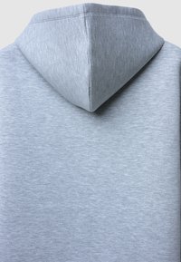 Felpa grigia chiaro con un tessuto morbido e testurizzato. Presenta un cappuccio a punta e un design minimalista, con cuciture visibili lungo i bordi.