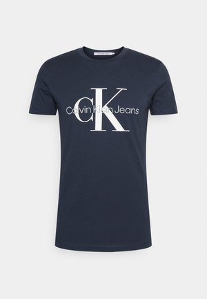 Temno modra bombažna majica s kratkimi rokavi z velikim belim "cK" in sivim napisom "Calvin Klein Jeans" na sredini spredaj.