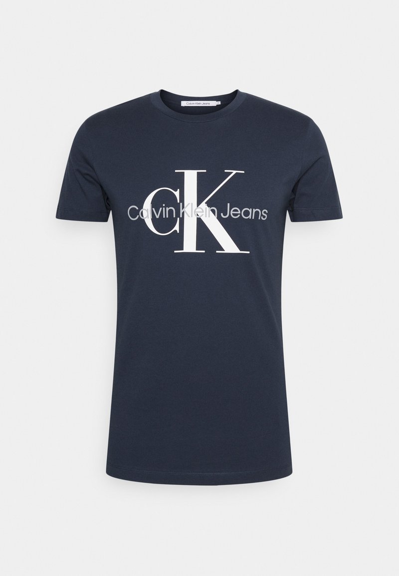 Tmavomodré bavlnené tričko s krátkym rukávom s veľkým bielym nápisom "cK" a sivým logom "Calvin Klein Jeans" v strede na prednej strane.