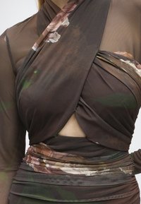Gros plan d'une personne portant un top cache-cœur marron transparent et une jupe froncée assortie avec des motifs floraux et une petite découpe au niveau du ventre.