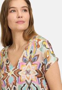 Bluse mit floralem Muster, V-Ausschnitt, kurzen Ärmeln, leichtem Stoff und einer Mischung aus Pastellfarben, darunter Rosa, Braun und Blau.