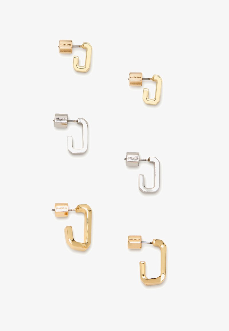 Två par geometriska örhängen i guld och silver. Varje par har en blockpost med varumärkesnamnet. Formerna är rundade och vinklade.