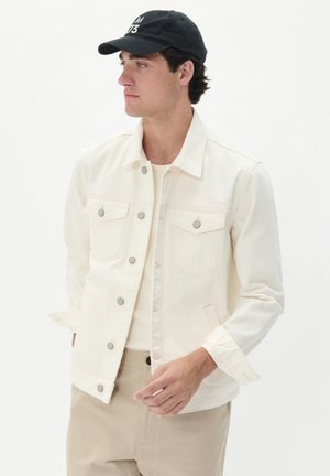 Witte denimjas met zilveren knopen, twee borstzakken en een klassieke kraag, gecombineerd met een lichtgekleurde blouse en beige broek.