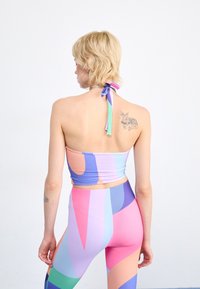 Farebný crop top s holými ramenami a geometrickými vzormi v ružovej, fialovej a modrej farbe, doplnený o zodpovedajúce legíny s vysokým pásom. Hladká textúra látky.