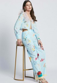 Blue cropped jacket with ruffled sleeves and colorful prints, paired with wide-leg pants featuring various illustrations and a chain accent.