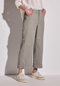Hellgraue, cropped Hosen mit einer taillierten Taille, Seitentaschen und weitem Bein. Glattes Material mit leichtem Glanz, kombiniert mit weißen Sneakers.