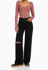 Rosa, geripptes Crop-Top mit langen Ärmeln und quadratischem Ausschnitt, kombiniert mit schwarzen, weit geschnittenen Jeans mit Rissen an den Knien und schwarzen Sneakers.