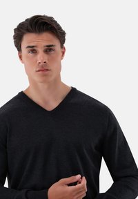 Schwarzer V-Ausschnitt-Pullover aus weichem Stoff. Figurschnitt mit langen Ärmeln. Glatte Textur und schlichte Verarbeitung ohne Muster oder Verzierungen.