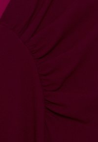Burgundy-kangas, jossa on pehmeä rakenne ja joka sisältää rypistystä sauman varrella, luoden hienovaraisia mutkia ja muotoilua.