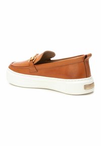 Zapato marrón de cuero tipo slip-on con suela de plataforma blanca, que presenta una solapa frontal y un detalle de hardware dorado. Textura suave y forma redondeada.
