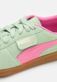 Baskets Puma Palermo vert menthe et rose avec texture en daim, bande rose, logo doré et semelle en caoutchouc marron.