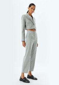 Blazer recortado de un gris claro con un solo botón, combinado con pantalones ajustados de gris claro. El conjunto presenta texturas sutiles y líneas limpias.