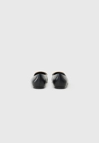 Ballerines en cuir noir avec un design à bout pointu, texture lisse et forme minimaliste. Pas de matériel ou de décorations visibles.