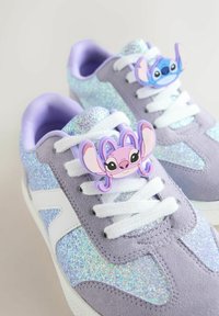 Purple and glittery sneakers with white laces, each featuring a cartoon character charm on the laces—pink and blue faces with large eyes.