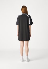 Czarna sukienka z krótkim rękawem o teksturowanym wzorze na rękawach, białych akcentach na ramionach oraz luźnym kroju. Noszona z białymi sneakersami.