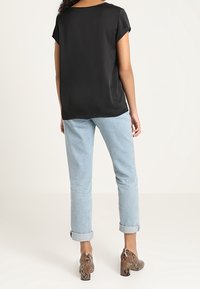 Blusa nera a maniche corte abbinata a jeans azzurri con risvolto e scarpe con tacco a stampa rettile. Tessuto liscio con una vestibilità comoda.