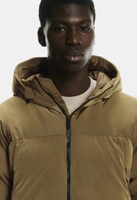 Khakifarbene Steppjacke mit Kapuze, Reißverschluss und glatter Textur. Verfügt über ein kontrastierendes Innenfutter und ein schlichtes, sauberes Design.