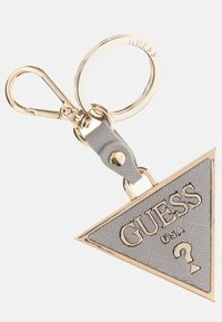 Portachiavi a forma di triangolo con superficie grigia texture, dettagli dorati e logo in rilievo "GUESS USA" con un dettaglio a forma di punto interrogativo. Finiture in metallo dorato.