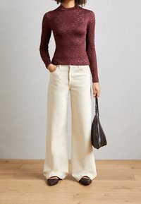 Burgundy ribbad långärmad topp med hög halsringning, i kombination med lösa, krämfärgade vida byxor och en liten svart handväska.