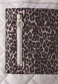 Tikkikuvioinen laukkuosio, jossa musta-beige leopardikuosi, hopeinen vetoketju ja vetonappi, valkoisen sileän materiaalin päällä.