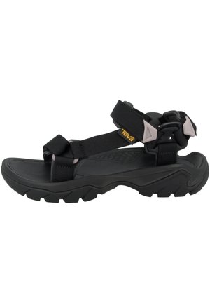 Sort udendørs sandal med justerbare stropper, tyk robust sål og et lille gult Teva-logo på sidespændet.