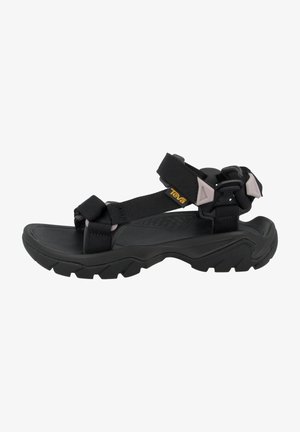 Sandale noire d'extérieur avec des sangles ajustables, une semelle épaisse et robuste, et un petit logo jaune Teva sur la bride latérale.
