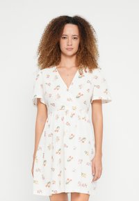 Λευκό φόρεμα με λουλούδια, V-λαιμόκοψη, κοντά μανίκια και σιλουέτα Α. Διακοσμημένο με πολύχρωμα λουλουδένια σχέδια σε όλη την επιφάνεια.