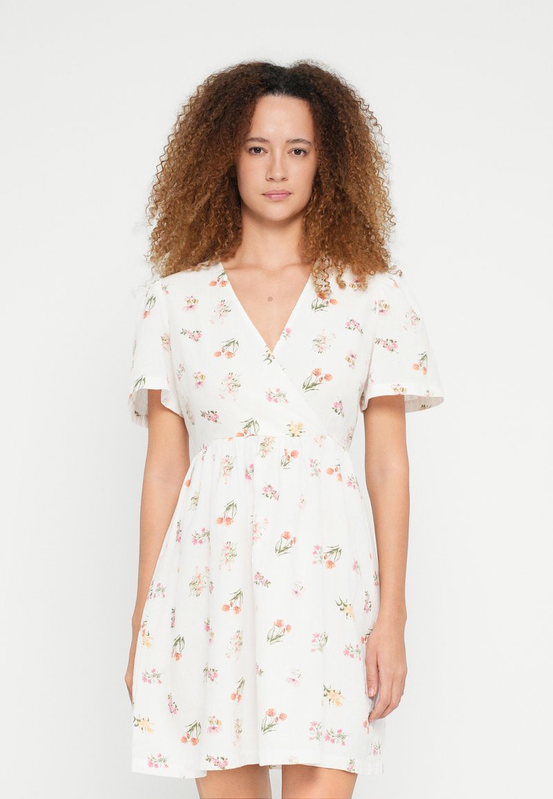 Λευκό φόρεμα με λουλούδια, V-λαιμόκοψη, κοντά μανίκια και σιλουέτα Α. Διακοσμημένο με πολύχρωμα λουλουδένια σχέδια σε όλη την επιφάνεια.