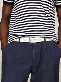 Person wearing navy pants with hands in pockets, white belt, and black-and-white striped shirt tucked in.