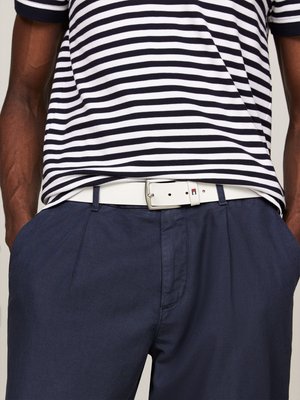 Person wearing navy pants with hands in pockets, white belt, and black-and-white striped shirt tucked in.