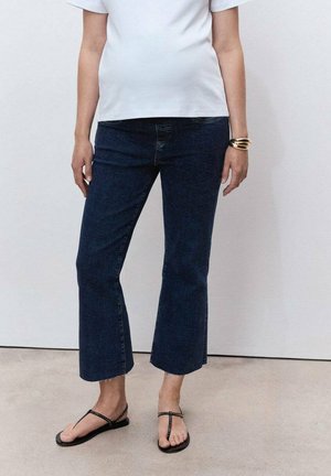 Dark blue cropped jeans with a straight leg cut, paired with black flip-flops featuring studded accents. White t-shirt with a relaxed fit.