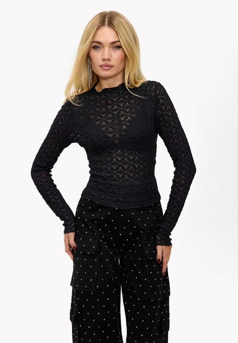 Haut noir à manches longues en dentelle texturée avec un motif géométrique ; associé à un pantalon noir à jambes larges avec des clous argentés et des poches.