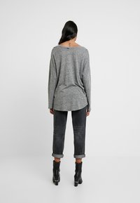 Graues Langarmoberteil mit lässiger Passform, abgerundetem Saum hinten und weichem Material, kombiniert mit dunklen, hochgerollten Jeans und schwarzen Stiefeletten.