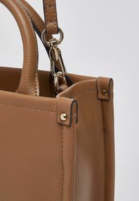 Sac à main en cuir marron avec une surface texturée, des ferrures dorées, et un design robuste et structuré avec deux poignées et une bandoulière amovible.