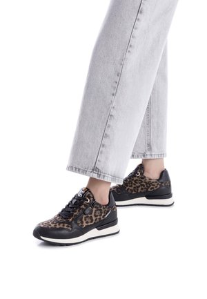 Zapatillas de animal print de leopardo con detalles de cuero negro, tela texturizada, diseño de lazada plana y suela blanca, combinadas con jeans de pierna ancha grises.