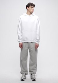 Valge kapuutsiga dressipluus esitaskuga, kombineeritud helehallide dressipükste ja hallide spordijalatsitega. Lihtne disain, vabaaja lõige.