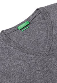Siwy sweter w serek wykonany z miękkiego materiału, z prążkowanym dekoltem i zieloną metką marki wszytą wewnątrz kołnierza.