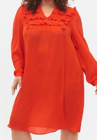 Robe rouge fluide en tissu léger ; dotée d'un col à volants et de manches longues avec poignets élastiques ; longueur au genou.