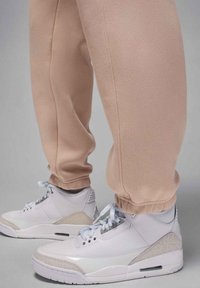 Białe trampki z szarymi akcentami, z perforowanymi detalami, w połączeniu z jasnoróżowymi spodenkami dresowymi z elastycznymi ściągaczami i miękką teksturą.