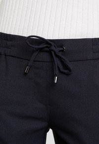 Marineblauwe broek van een gestructureerde stof, met een drawstringsluiting met metalen uiteinden en zijzakken.