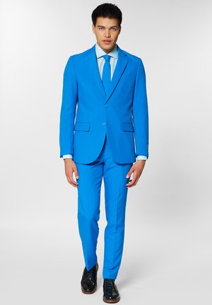 Jasnoniebieski garnitur z gładkiego materiału, z dwoma guzikami, dopasowanym krawatem i jasnoniebieską koszulą. Czarne eleganckie buty dopełniają strój.