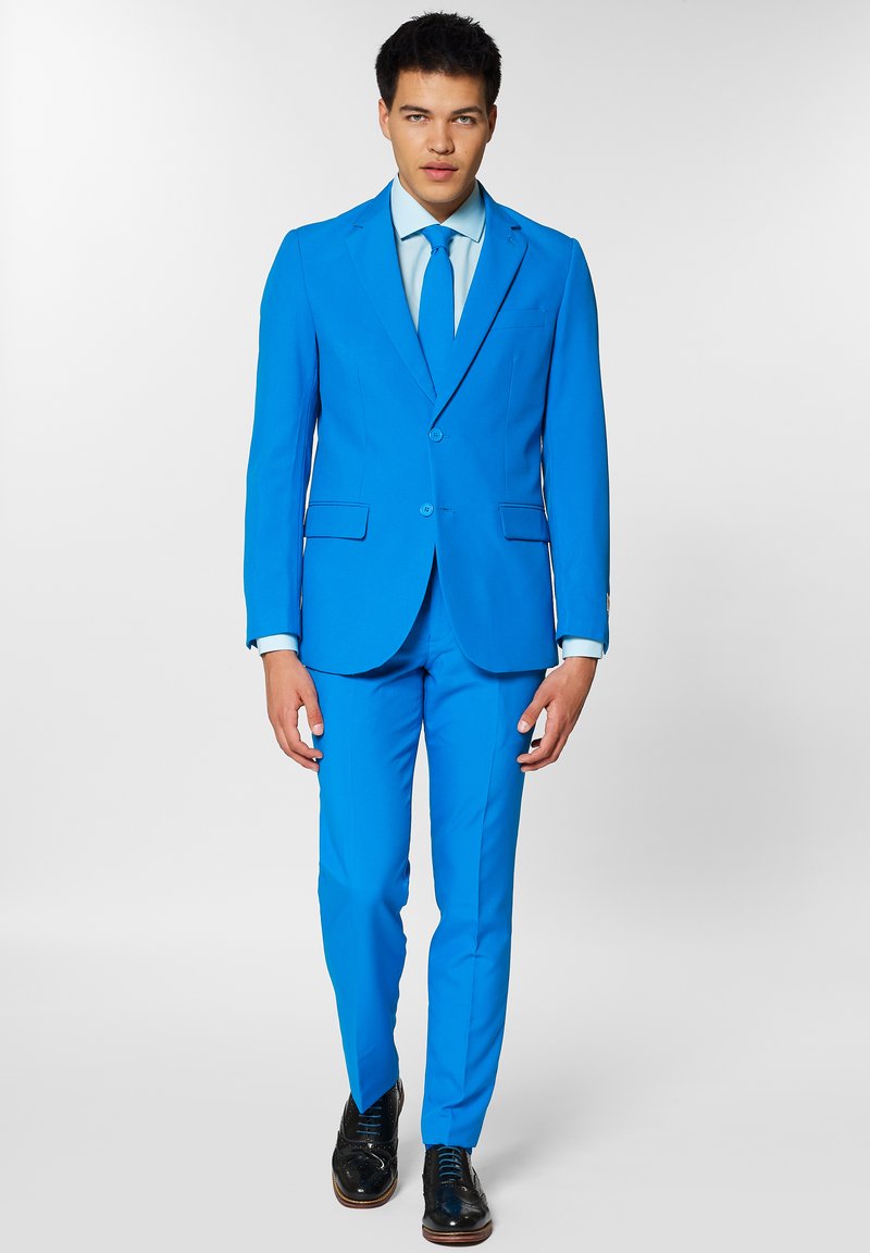 Traje azul brillante hecho de una tela suave con dos botones, corbata a juego y una camisa azul clara. Zapatos de vestir negros completan el atuendo.