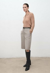 Suéter de punto beige con cuello, pantalones cortos grises claros a medida y botas negras de tacón alto hasta la rodilla, con un cinturón delgado. Texturas suaves.