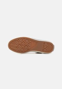 Semelle de sneaker en caoutchouc marron avec des lignes diagonales et des motifs en diamant. Cerclage blanc autour du bord, accent noir près du talon. Texturée pour une meilleure adhérence.