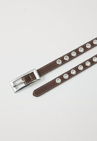 Brown leather belt with silver hardware, featuring several metal grommet holes for adjustment, and contrasting white stitching.