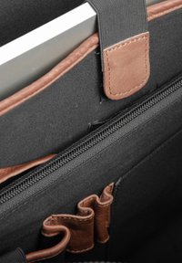 Intérieur d'un sac en tissu noir avec un accent en cuir marron, comportant une fermeture éclair et plusieurs boucles pour l'organisation. Un carnet est partiellement visible.