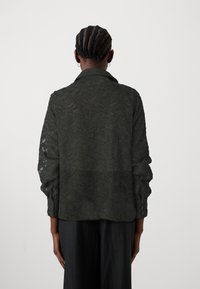 Σκούρο πράσινο διάφανο μπλουζάκι με λουλουδάτη υφή, μακριά μανίκια και κουμπωτές μανσέτες. Διαθέτει κλασικό γιακά και άνετη εφαρμογή.