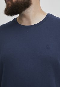 T-shirt di cotone blu navy con scollatura tonda e logo ricamato discreto sul petto, caratterizzato da una texture liscia e maniche corte.