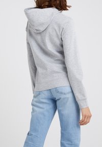 Gray cotton hoodie with a lined hood, relaxed fit, and long sleeves. Paired with light blue denim jeans displaying a classic five-pocket design.