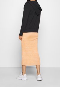 Svart hoodie med huva, kombinerad med en knälång, texturerad orange stickad kjol. Vita sneakers fulländar outfiten.